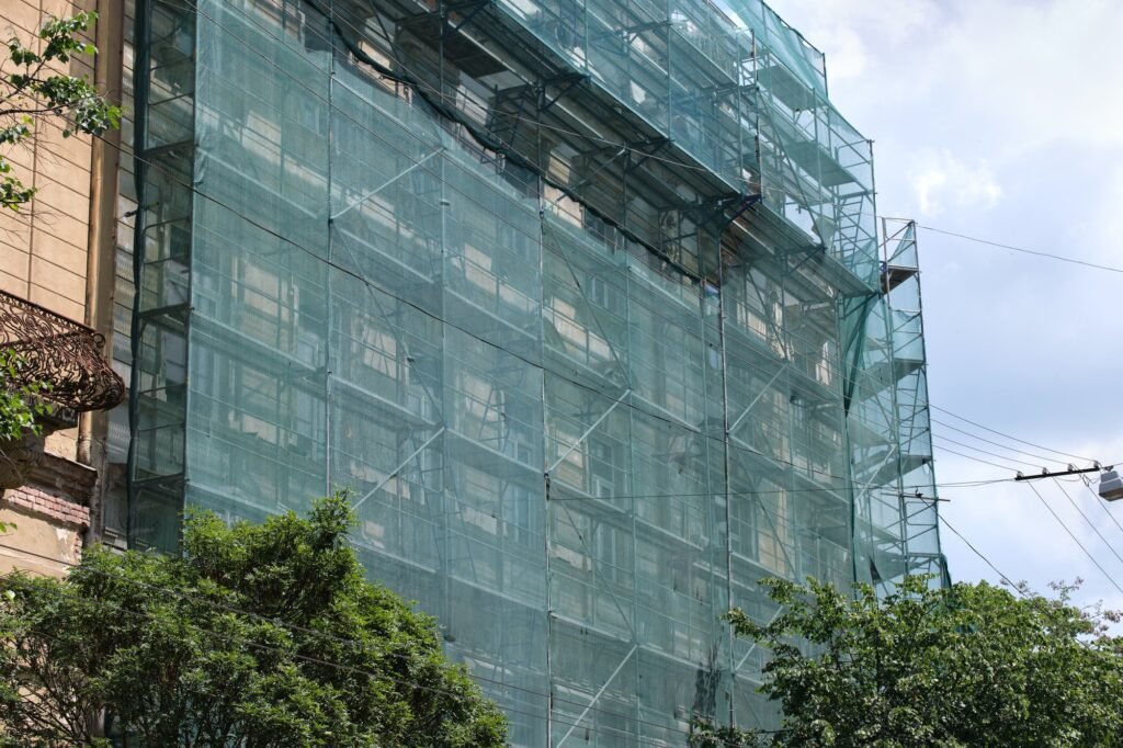 Building facade under renovation works with construction scaffolding frame covered with protective